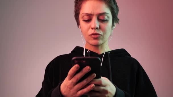 Short haircut girl listens to music and clicks smartphone — Stock Video