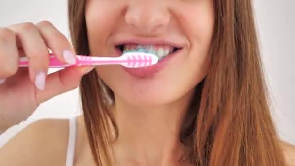 Close-up portret van een jonge vrouw die poetst haar tanden na wakker worden op een witte achtergrond na. Hygiëne concept. 4k — Stockvideo