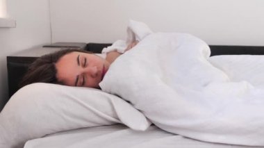 Tembel hafta sonu uyanıyor, genç yetişkin bir kadın yatağından kalkmak istemiyor, beyaz yatak odası sabah güneşiyle aydınlanıyor. Kız aylak aylak dolaşıyor ve yumuşak bir yerden ayrılmak istemiyor. 4k