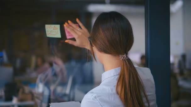 迷人的女商人在玻璃白板上使用贴纸集思广益解决问题的策略，为办公室会议的最后期限展示解决方案 — 图库视频影像