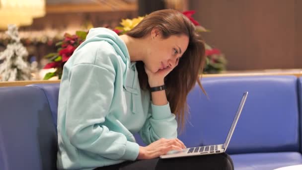 Μια νεαρή γυναίκα σε ένα φούτερ αναπτύσσει μια εφαρμογή, χαμογελάει κλικ σε ένα φορητό υπολογιστή και το δοκιμάζει 4k — Αρχείο Βίντεο