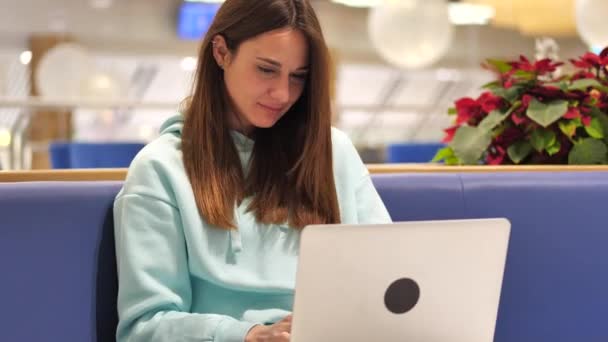 Mujer joven en una sudadera desarrolla una aplicación, hace clic en un ordenador portátil y lo prueba 4k — Vídeo de stock