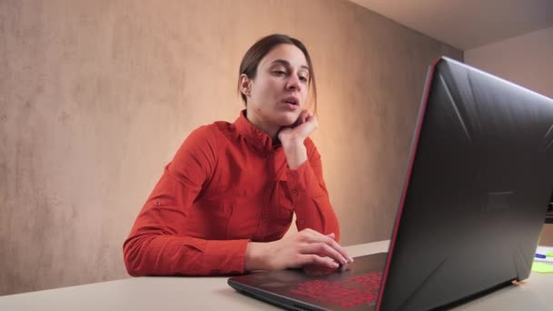 Retrato de una chica gerente de ventas. Su cabello está en la cola de su camisa naranja. Mujer sentada en un ordenador portátil y tomando café. 4k — Vídeo de stock