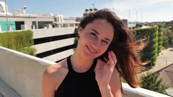 Aantrekkelijke vrouw op een dakterrein van een winkelcentrum Urban city achtergrond. Ze glimlacht en haar haren fladderen in de wind. 4k — Stockvideo