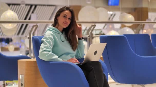 Young woman sits in the lobby and looks at the laptop screen. She smiles and rejoices 4k — Stock Video