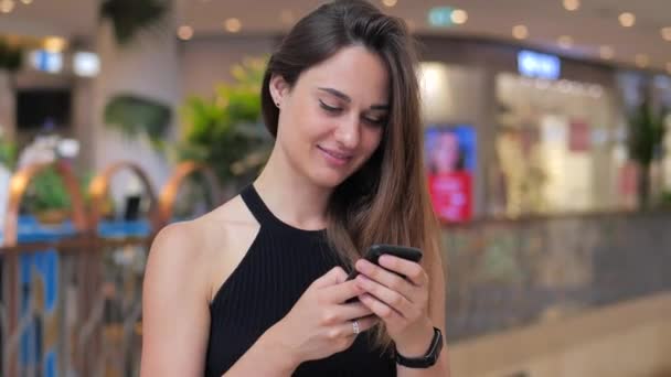 La joven señorita está escribiendo mensajes en su teléfono móvil que se encuentra dentro del centro comercial. 4k — Vídeos de Stock