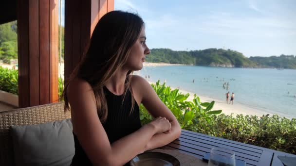 Menina atraente está sentado no café com vista para o mar. 4k — Vídeo de Stock