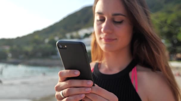 Retrato de uma menina no fundo de uma casa de campo no oceano .Paisagem exótica. Ela clica nos botões de seu smartphone. Conceito de férias 4k — Vídeo de Stock