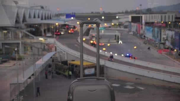 Egy bőrönd kihúzható fogantyúval. Poggyásztáska a reptéren egy homályos ablaknak támasztva. 4k — Stock videók