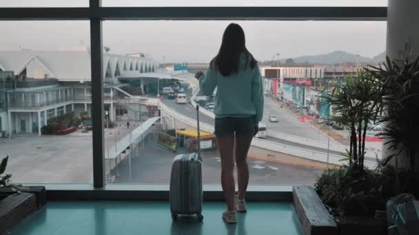 Молодая девушка ждет своего рейса у окна в аэропорту с мешком в руках — стоковое видео