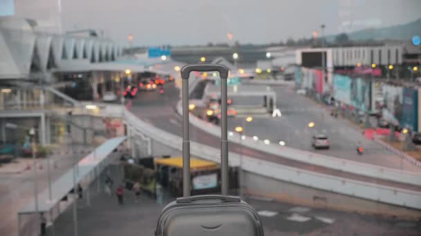 Egy bőrönd kihúzható fogantyúval. Poggyásztáska a reptéren egy homályos ablaknak támasztva. 4k — Stock videók