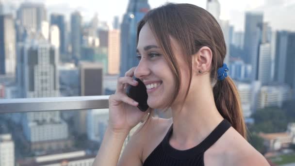 Закрытая деловая занятая девушка разговаривает по телефону на фоне небоскребов. 4k — стоковое видео