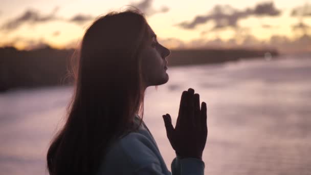 Krásná dívka modlí se dívá na oranžovou oblohu s nadějí, zblízka. Silueta mladé ženy, která snila o tom, jak se dívá ven na západ slunce. 4k — Stock video