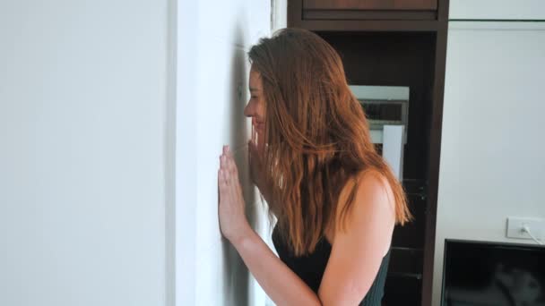 Paranoid woman is shocked looking into the peephole. The female wants to hide from an unexpected guest and shows shh. 4k — Stockvideo