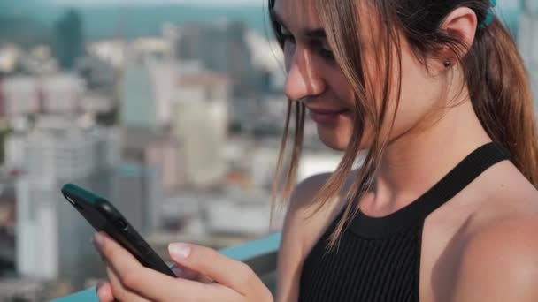 Primer plano de negocios chica ocupada con los hombros abiertos. Mujer joven hace clic en los botones del teléfono de los rascacielos en el fondo. 4k — Vídeos de Stock