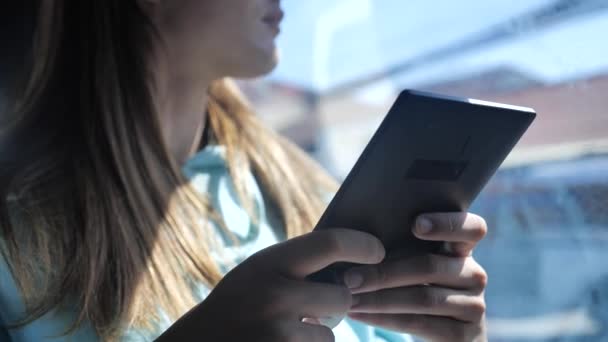 Młoda kobieta czyta książkę elektroniczną w autobusie. W oknie słoneczny dzień, palmy na tle 4k — Wideo stockowe