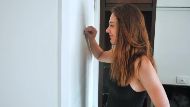 Paranoid woman is shocked looking into the peephole. The female wants to hide from an unexpected guest and shows shh. 4k — Stock Video