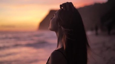 Sunset above ocean. Young woman standing on a beach and rises hands. 4k