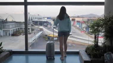 young girl is waiting for her flight near the window at the airport with baggage 4k