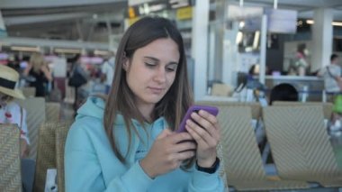 young woman is waiting for her fligh in airport. Female click on smartphone 4k