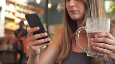 Bir kızın yakın plan portresi. Kadın bir kokteyl içiyor ve akıllı telefon 4K 'yı alkışlıyor.