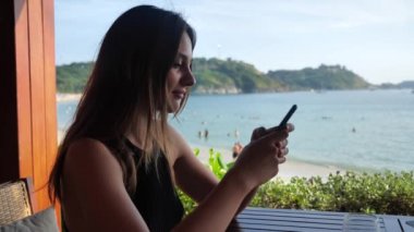 Gülümseyen, koyu kahverengi gözlü, siyah elbiseli, zarif, çekici genç kızın yakın plan fotoğrafı. Şehir geçmişiyle eğlenceli bir şeyler satın almaya çalışıyor.