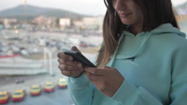 Брюнетка бокового вида, пользующаяся смартфоном у окна аэропорта. Девушка пишет сообщение с видом на задний план самолета. 4k — стоковое видео