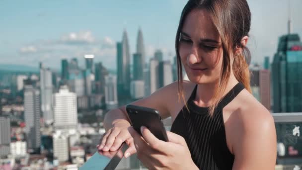 Close -up business busy girl with open shoulders. Young woman clicks on the phone buttons of skyscrapers on the background. 4k — 비디오