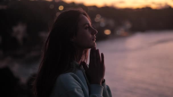 Beautiful woman praying looking up at purple sky with hope, close-up. Silhouette of young woman dreaming looking upwards sunset outdoors. 4k — Stockvideo