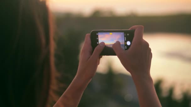拍摄年轻女子的近景，拍摄美丽的落日照片和录像。迷人的女性在日落时站在海滨拍照。女子在日落时拍照4k — 图库视频影像