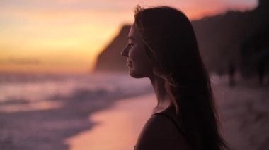 Sunset above ocean. Young woman standing on a beach and rises hands. 4k