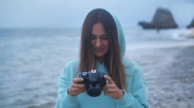 Portre hippi kadın elinde kamera olan profesyonel bir fotoğrafçı. Alacakaranlıkta okyanus arka planında fotoğraf çekiyor. 4k