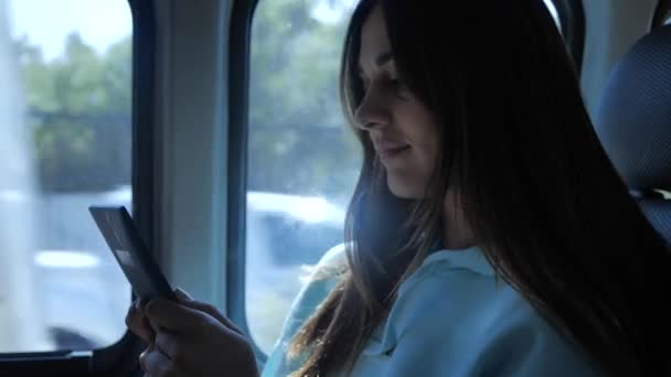 젊은 여성 이 버스를 타고 여행하며 전자책을 읽고 있습니다. 여자 아이가 4K 창문 앞에서 차를 타고 가고 있어요 — 비디오