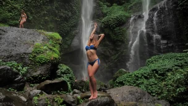 La silhouette d'une jeune femme dans une forêt tropicale sur fond de cascade se dresse sous la pluie. Unité avec la nature 4k — Video
