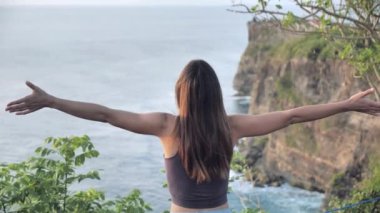 Turuncu gökyüzüne umutla bakan güzel bir kız, yakın plan. Genç bir kadının silueti okyanusun arka planında gün batımını seyrediyor..