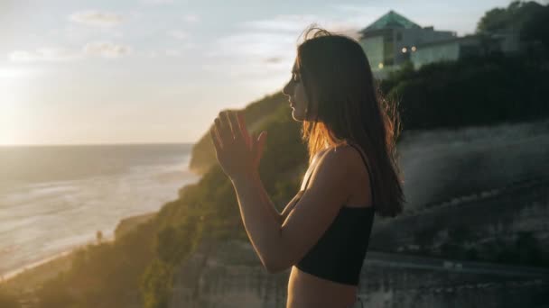 希望を持ってオレンジの空を見上げて祈る平和的な女の子、クローズアップ。Silhouetteの若いです女性の夢上方夕日屋外海の背景4k. — ストック動画