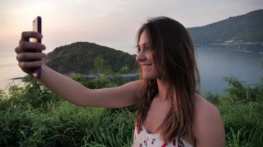 Güzel bir arka planda, çekici bir kadının yakın plan portresi. Dişi, dağların tepesinde gün batımını fotoğraflıyor. Doğada ruhani bir anın tadını çıkarıyor.