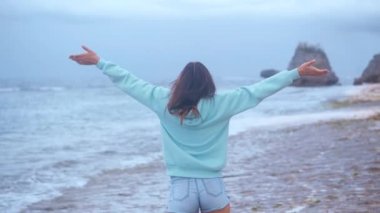 Güzel genç bir kadının portresi yaklaşır rüzgar gibi kollarını kaldırır, saçlarını savurur ve günbatımında huzurlu bir sahil kenarında eğlenir.