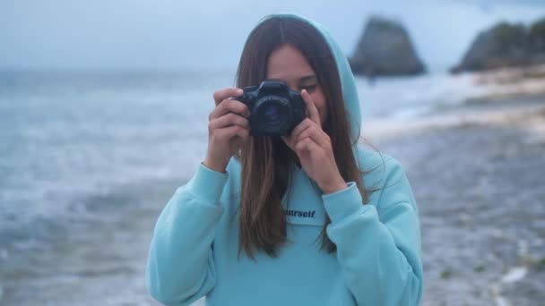 ポートレートヒップスター女性はカメラ付きのプロの写真家です。夕暮れ時に海を背景に写真を撮る。4k — ストック動画