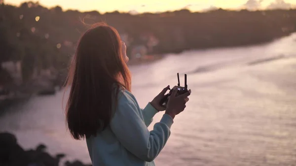Gün batımında okyanus yakınında uzaktan kumandalı mutlu genç kız kuadkopter drone 'u kontrol ediyor.