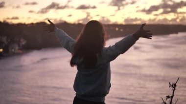 Güzel genç bir kadının portresi yaklaşır rüzgar gibi kollarını kaldırır, saçlarını savurur ve günbatımında huzurlu bir sahil kenarında eğlenir.