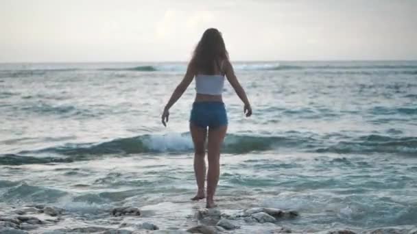 Una chica en el océano levanta las manos, admira las olas. 4k — Vídeo de stock