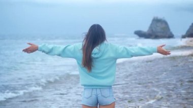 Güzel genç bir kadının portresi yaklaşır rüzgar gibi kollarını kaldırır, saçlarını savurur ve günbatımında huzurlu bir sahil kenarında eğlenir.