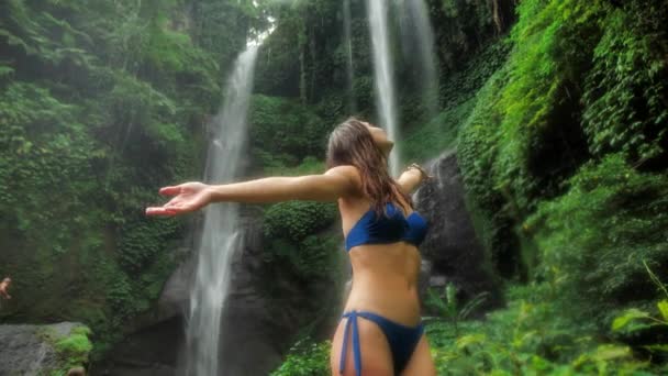 Красивая женщина в купальнике с распростертыми объятиями на фоне водопада Sekumpul. 4k — стоковое видео