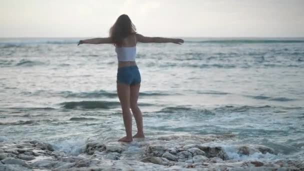 Una chica en el océano levanta las manos, admira las olas. 4k — Vídeos de Stock