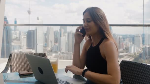 Mujer de negocios de confianza está trabajando en un ordenador portátil que habla por teléfono en la terraza del centro de negocios. Mujer hermosa con estilo hace un trabajo importante. Gran distrito de negocios de la ciudad urbana — Vídeos de Stock