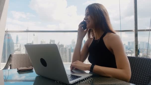 Mujer de negocios segura sentada en un café al aire libre hablando por teléfono. La hora del almuerzo. Gran distrito de negocios de los rascacielos fondo 4k — Vídeo de stock