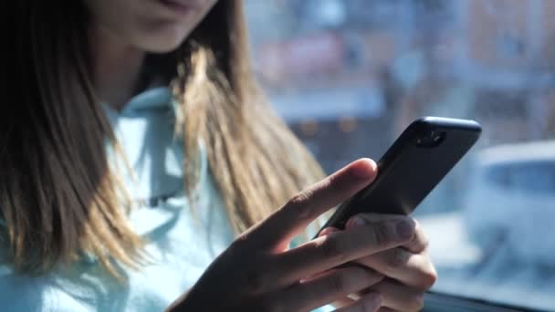 Una mujer joven está haciendo clic en el teléfono inteligente en un autobús. En la ventana un día soleado, palmeras en el fondo 4k — Vídeo de stock