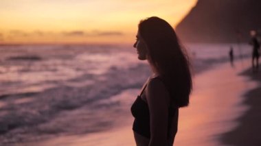 Okyanusun üstünde gün batımı. Zarif bir kadın kumsalda duruyor ve elini kaldırıyor. 4k