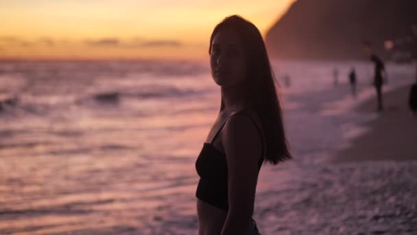 Anmutige Frau schaut in die Kamera und genießt den lila Sonnenuntergang. Urlaubskonzept 4k — Stockvideo